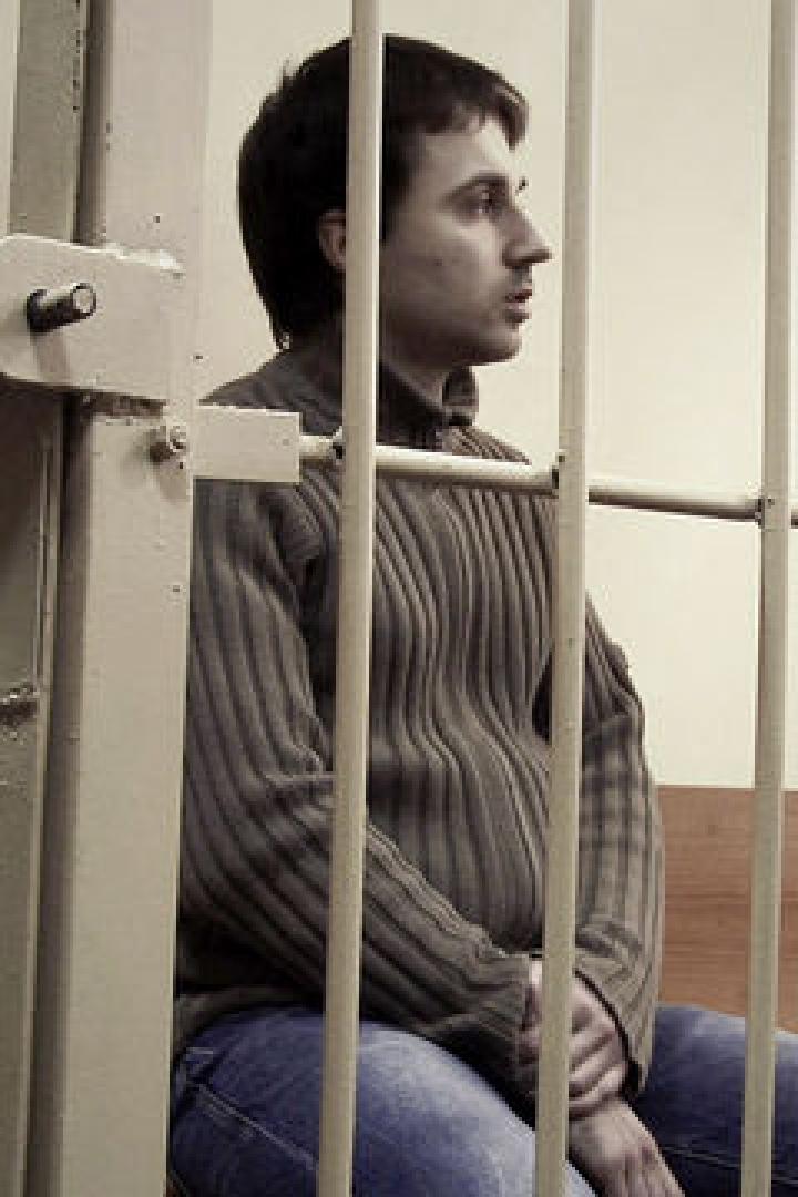 Ein Mann sitzt in einer Gefängniszelle hinter Gittern.