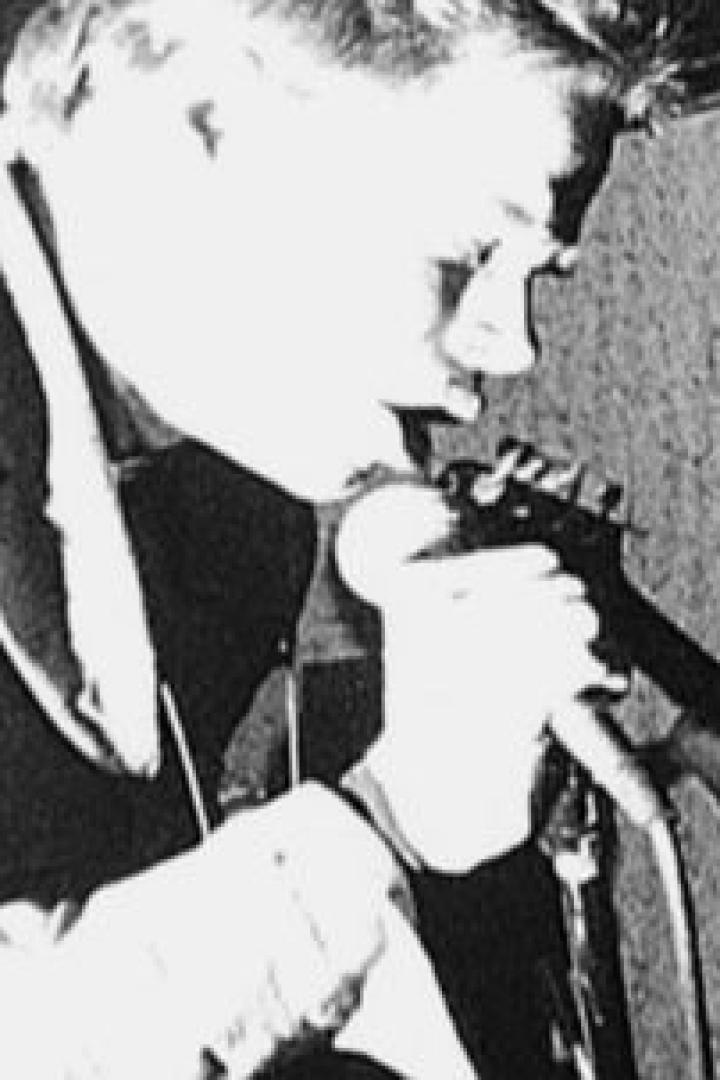 Ein Sänger singt in ein Mikrofon, während ein Gitarrist im Hintergrund spielt.