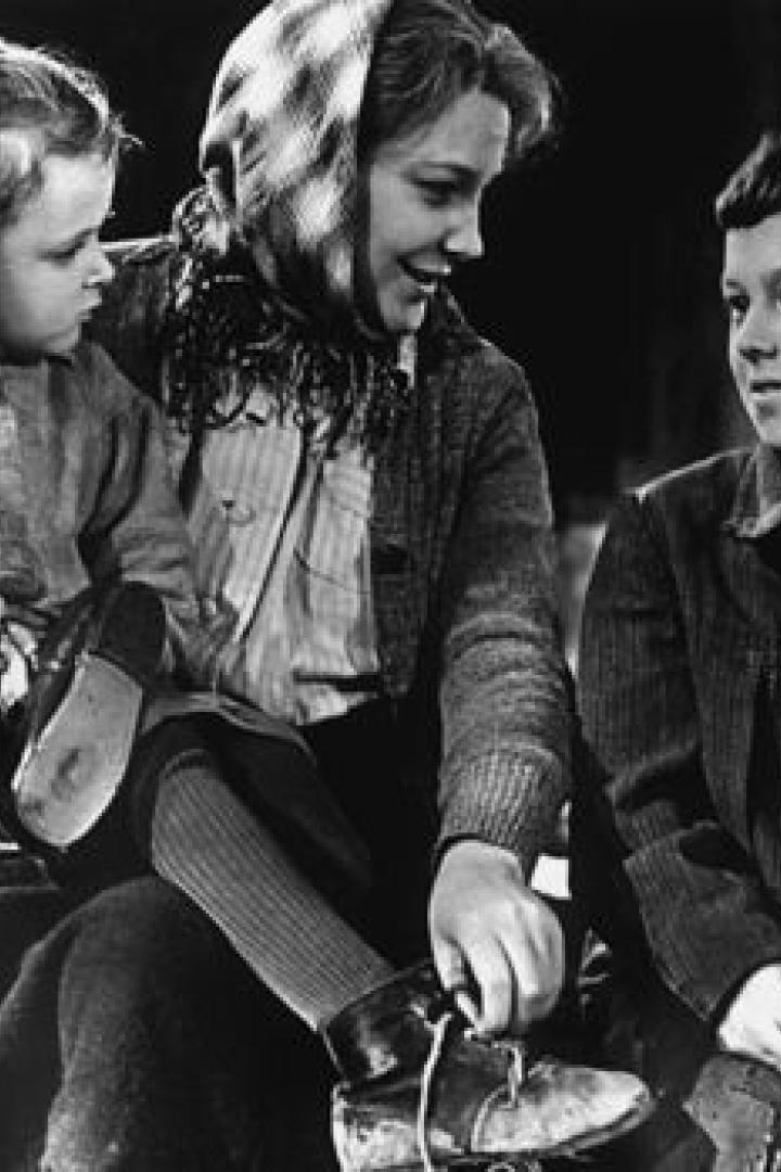 Eine Frau sitzt mit zwei Kindern, während sie einem von ihnen die Schuhe bindet.