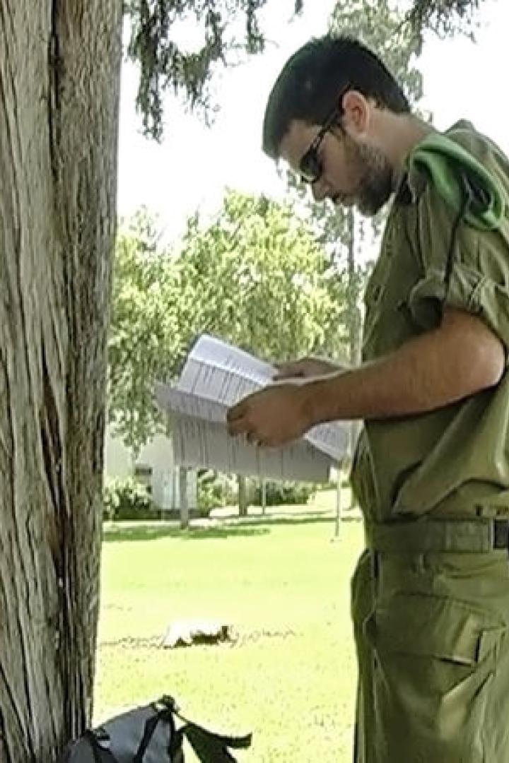 Ein Soldat in Uniform liest ein Dokument im Freien, mit einem Gewehr über der Schulter.
