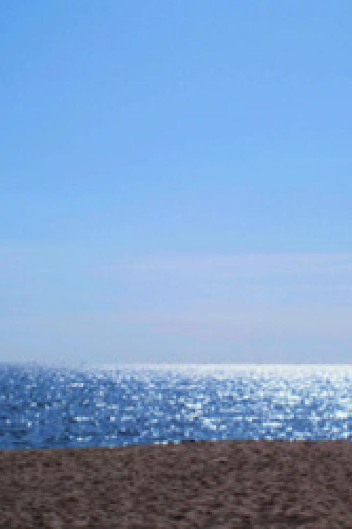 Zwei Personen stehen am Strand und blicken auf das glitzernde Meer.