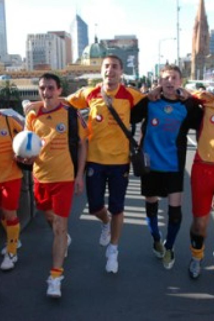 Eine Gruppe von Fußballspielern in gelb-roten Trikots geht über eine Brücke in einer Stadt.