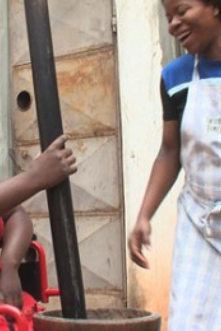 Eine Frau im Rollstuhl und eine Frau mit Schürze lachen zusammen, während sie traditionell kochen.