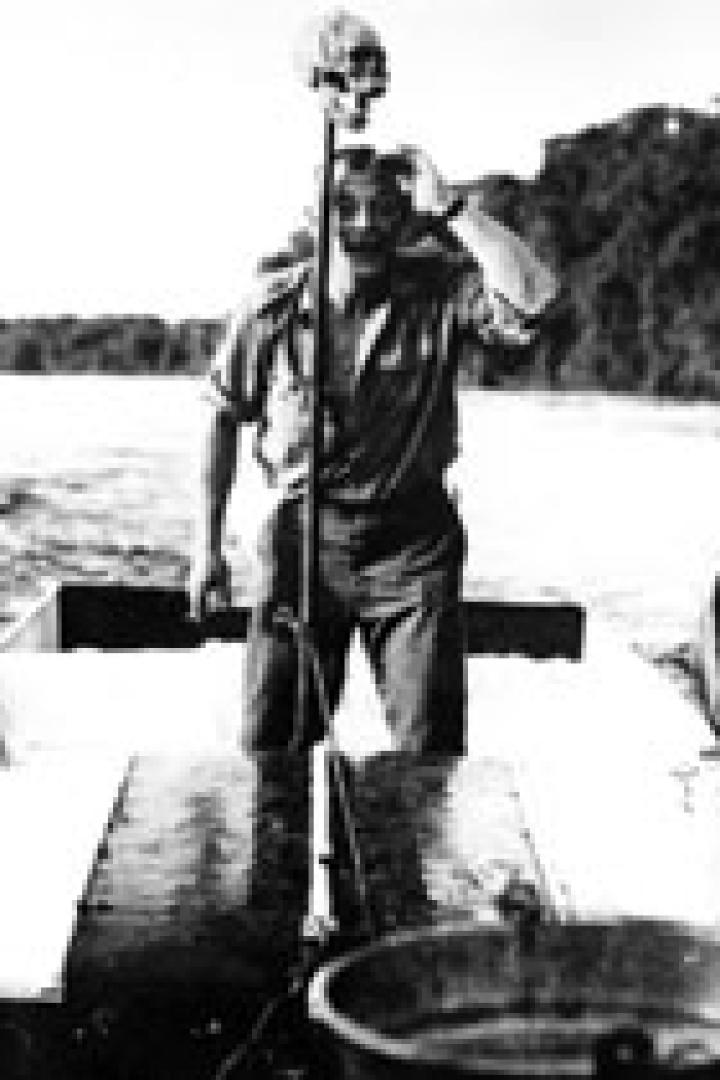 Ein Mann steht in einem kleinen Boot auf einem See und winkt.