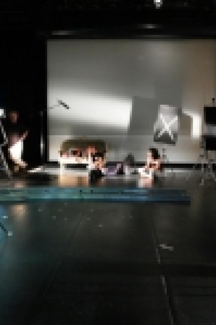 In einem Filmstudio sitzen zwei Personen vor einer Leinwand, umgeben von Filmtechnik.