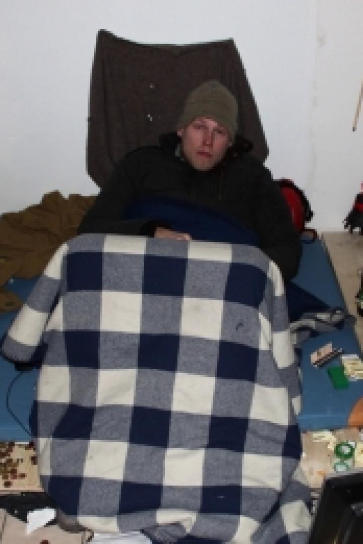 Ein Mann liegt in einem unordentlichen Raum auf einer Matratze.