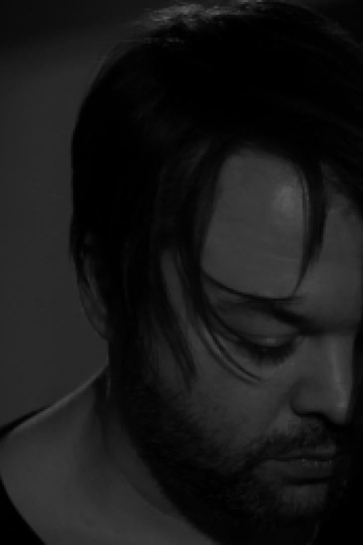 Ein Mann mit dunklen Haaren und Bart blickt nach unten.