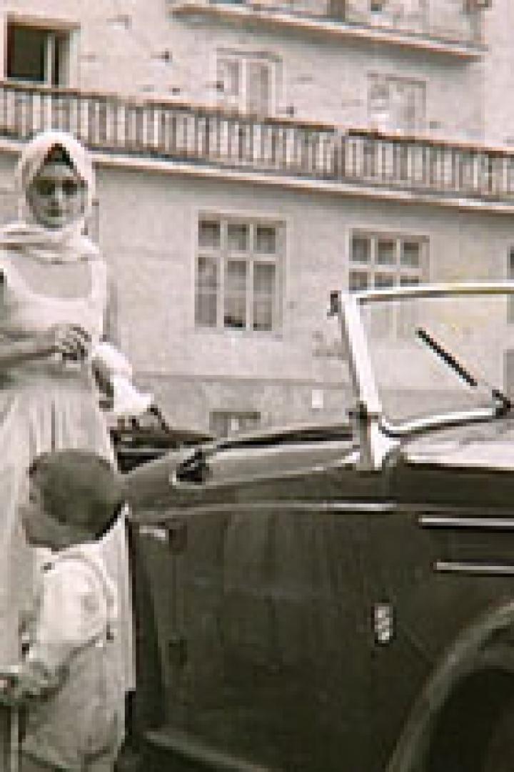 Eine Familie steht neben einem Oldtimer-Cabriolet auf einer Straße.