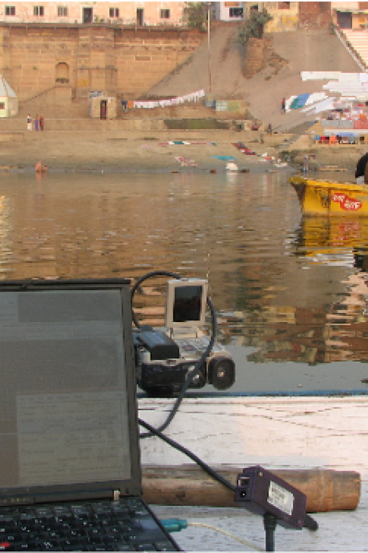Ein Laptop und Messgeräte auf einem Boot vor der Kulisse von Varanasi am Ganges.