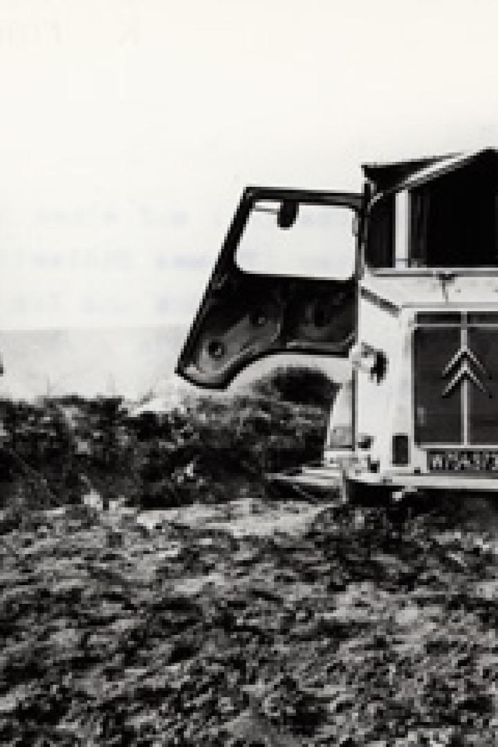 Ein Mann trägt Säcke an einem Strand, während ein Citroën-Lieferwagen im Sand steckt.
