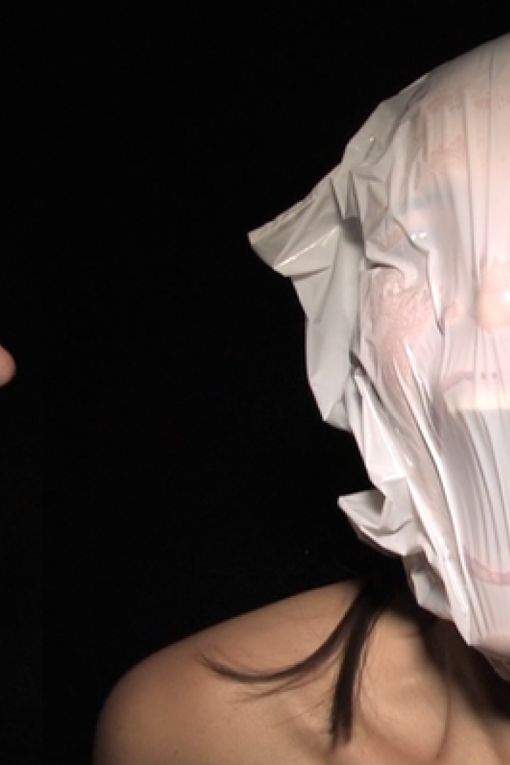 Eine Frau blickt auf eine andere Frau, deren Kopf in einer Plastiktüte steckt.