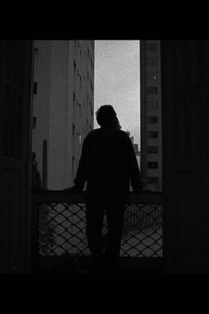 Eine Person steht in einer dunklen Wohnung am Fenster und blickt auf die gegenüberliegenden Gebäude.