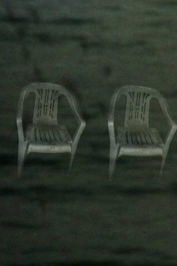 Vier leere Plastikstühle stehen im Dunkeln nebeneinander.