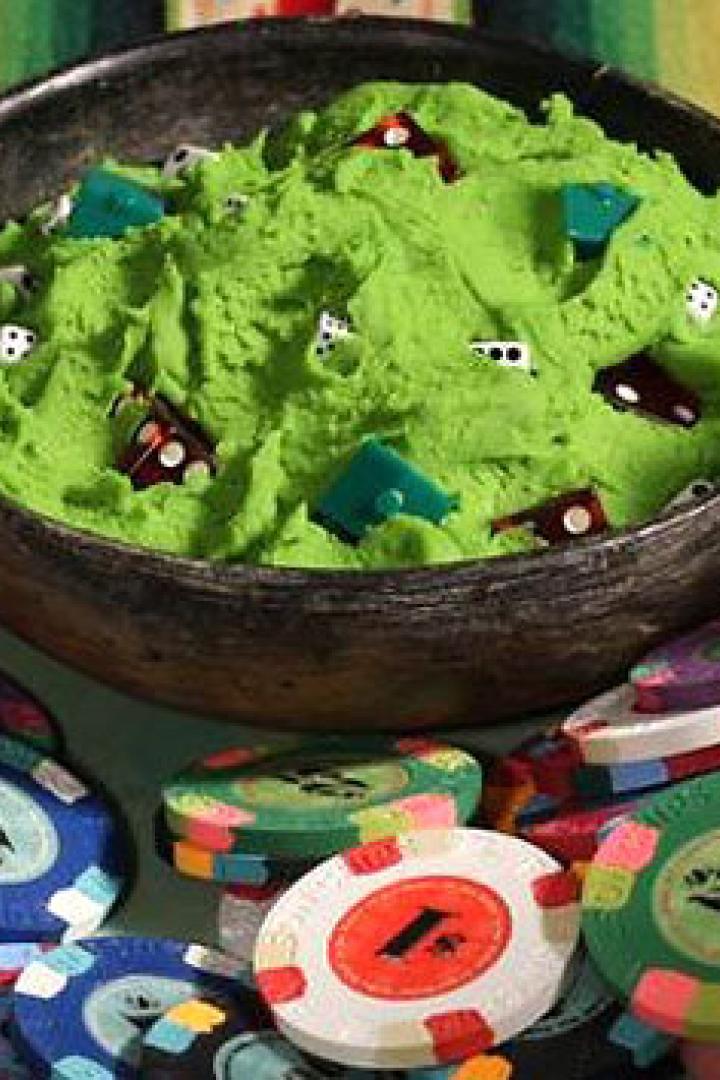 Ein Teller mit Spielchips und eine Schüssel mit grünem Teig, dekoriert mit Würfeln und Spielhäusern.