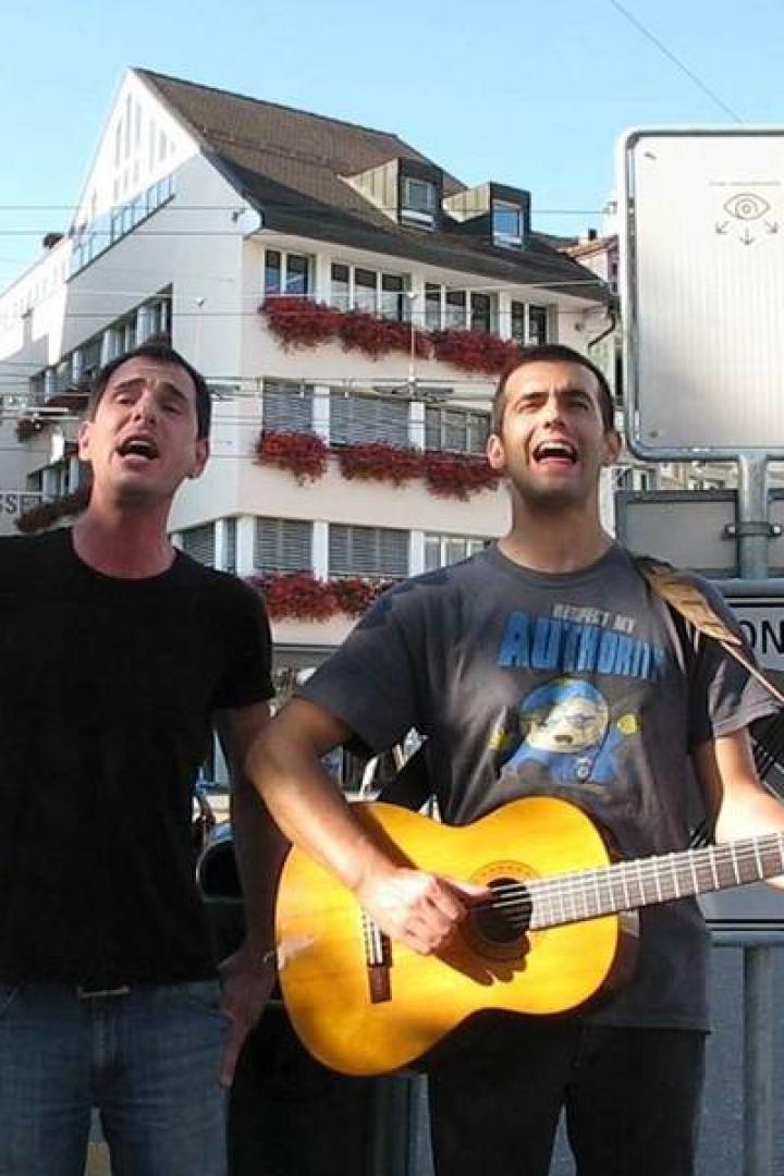 Zwei Männer stehen auf einer Straße und singen, einer spielt Gitarre.