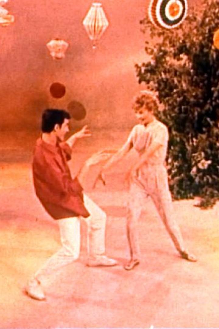 Ein Mann und eine Frau tanzen vor einem orangefarbenen Hintergrund mit Dekorationen.