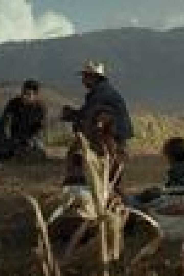 Eine Gruppe von Menschen sitzt auf einem Feld vor einer Bergkulisse.