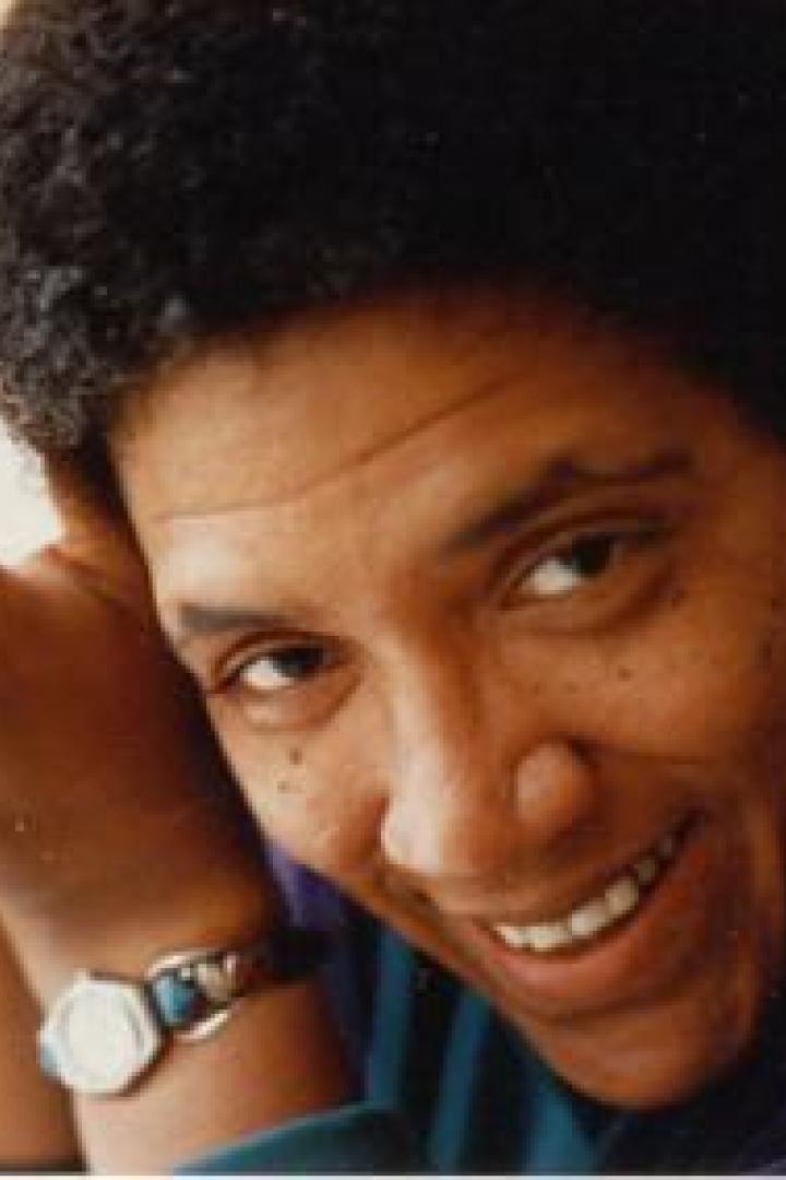 Eine lächelnde Frau mit dunklen Haaren hält eine Tasse in ihren Händen.