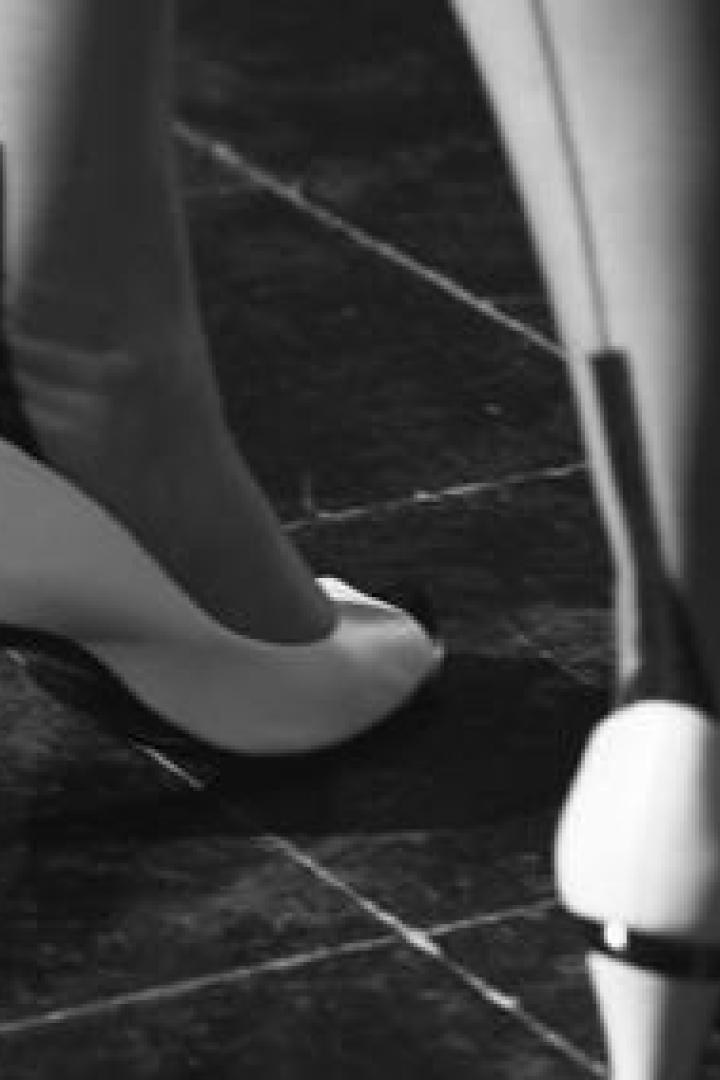 Nahaufnahme von Beinen in Strümpfen und weißen Schuhen mit Absatz auf einem gefliesten Boden.