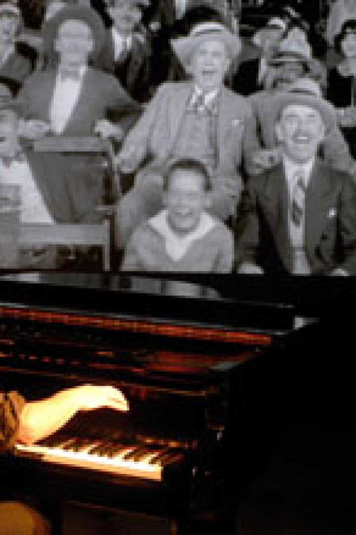 Ein Pianist spielt vor einer Leinwand, auf der eine Schwarzweißaufnahme von lachenden Menschen zu sehen ist.