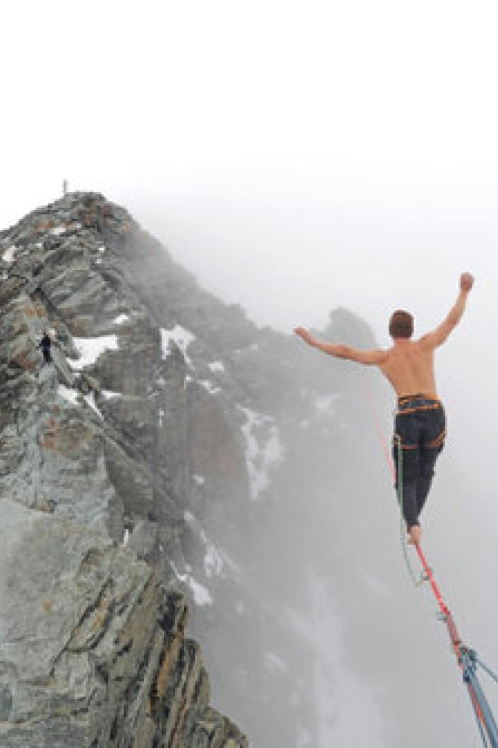 Ein Mann balanciert auf einer Slackline zwischen zwei Berggipfeln.