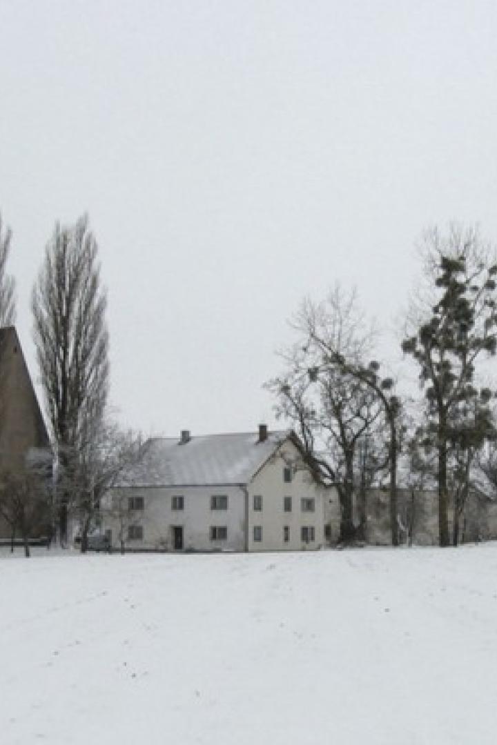 Eine verschneite Landschaft mit einer Kirche und einigen Häusern.