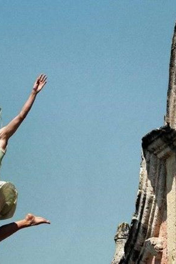 Eine junge Frau springt barfuß vor einem alten Gebäude in die Luft.