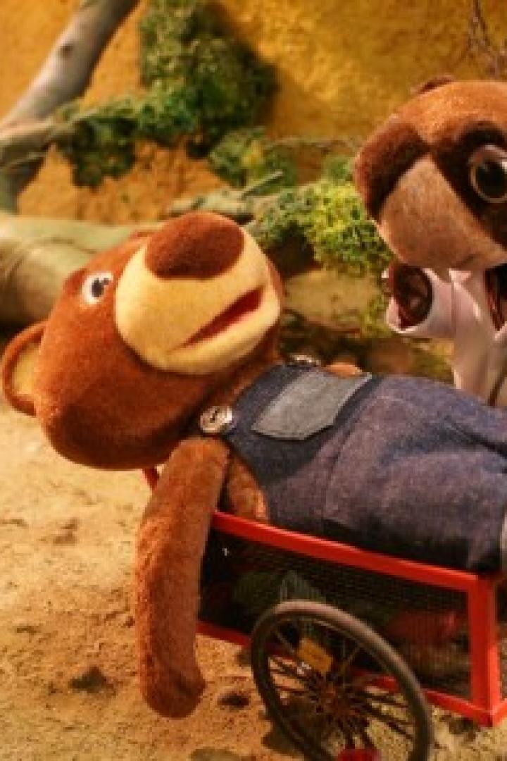 Ein Bär liegt in einem Wagen, während ein Dachs im Arztkittel daneben steht.