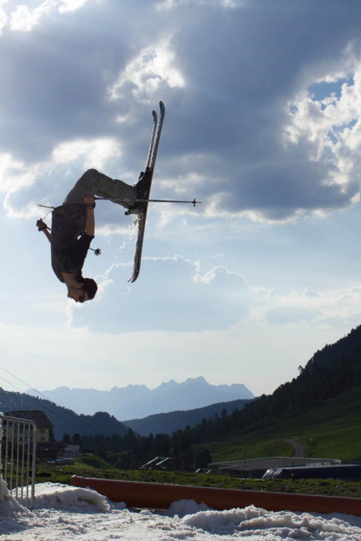 Ein Skifahrer macht einen Rückwärtssalto in der Luft vor einer Bergkulisse.