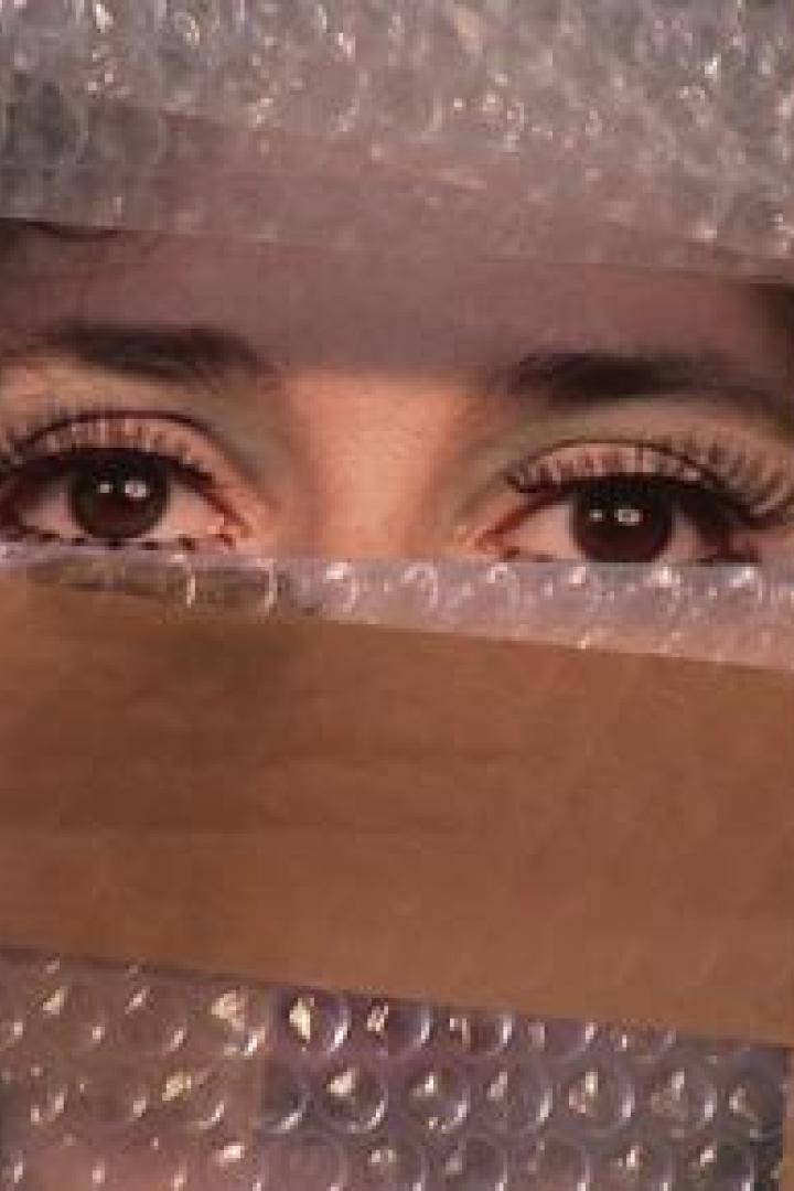 Ein Paar Augen blickt durch eine Verpackung aus Luftpolsterfolie und Klebeband.