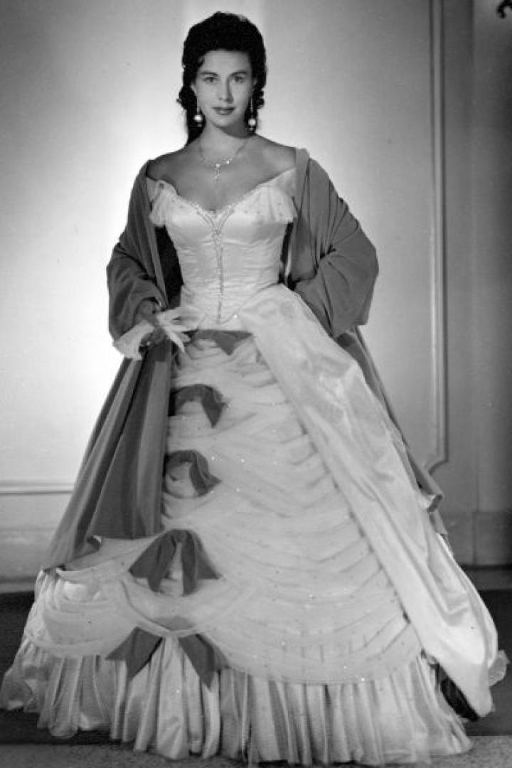 Eine Frau in einem eleganten Ballkleid mit Schleifen und einem Tuch über den Schultern.