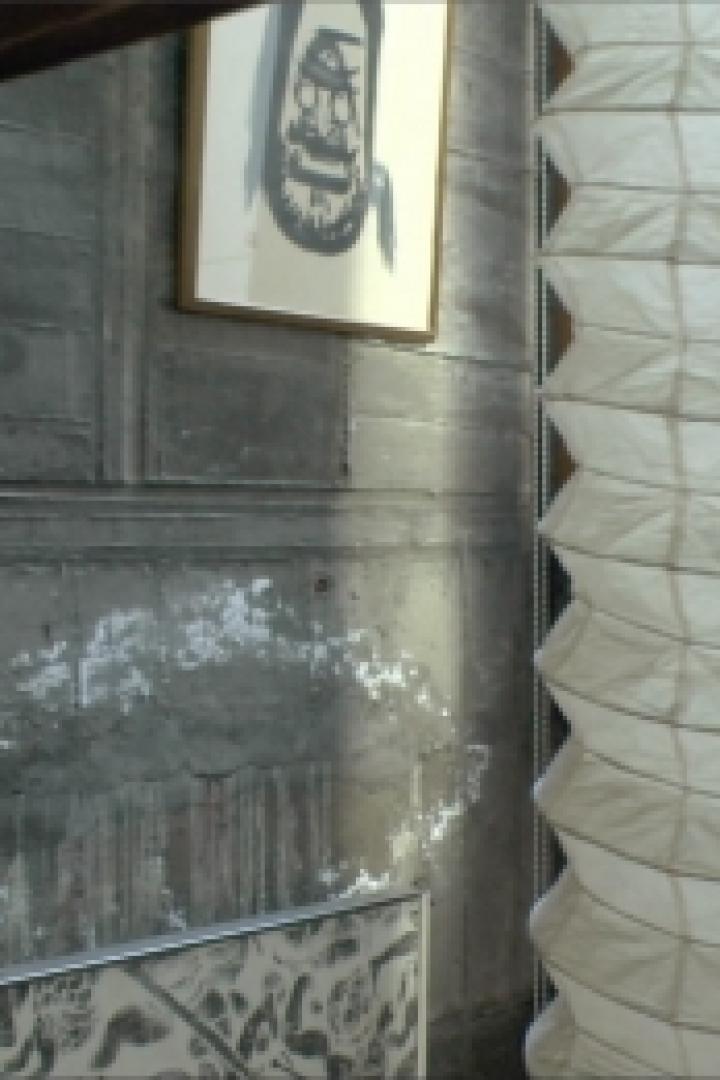 Eine spiralförmige Papierlaterne hängt vor einer grauen Wand mit einem Bild.