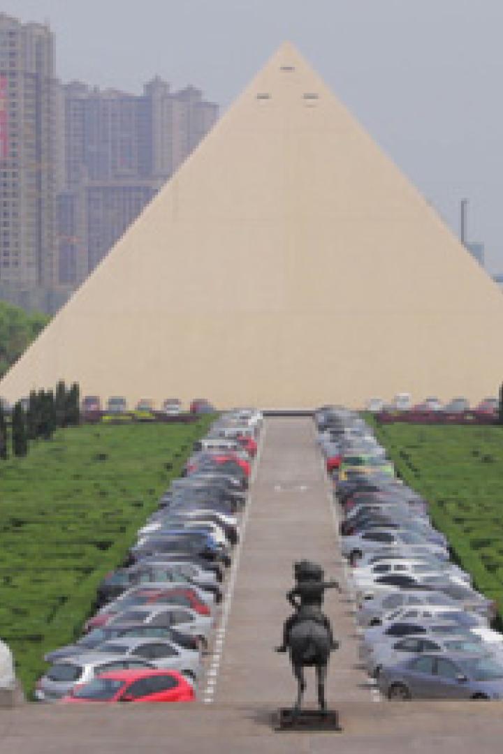 Eine große Pyramide dient als Hintergrund für einen Parkplatz voller Autos.