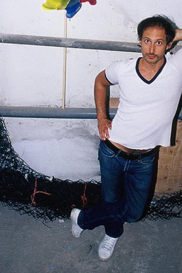 Ein Mann posiert lässig in einem Kellerraum mit Rohren und einer Tür.