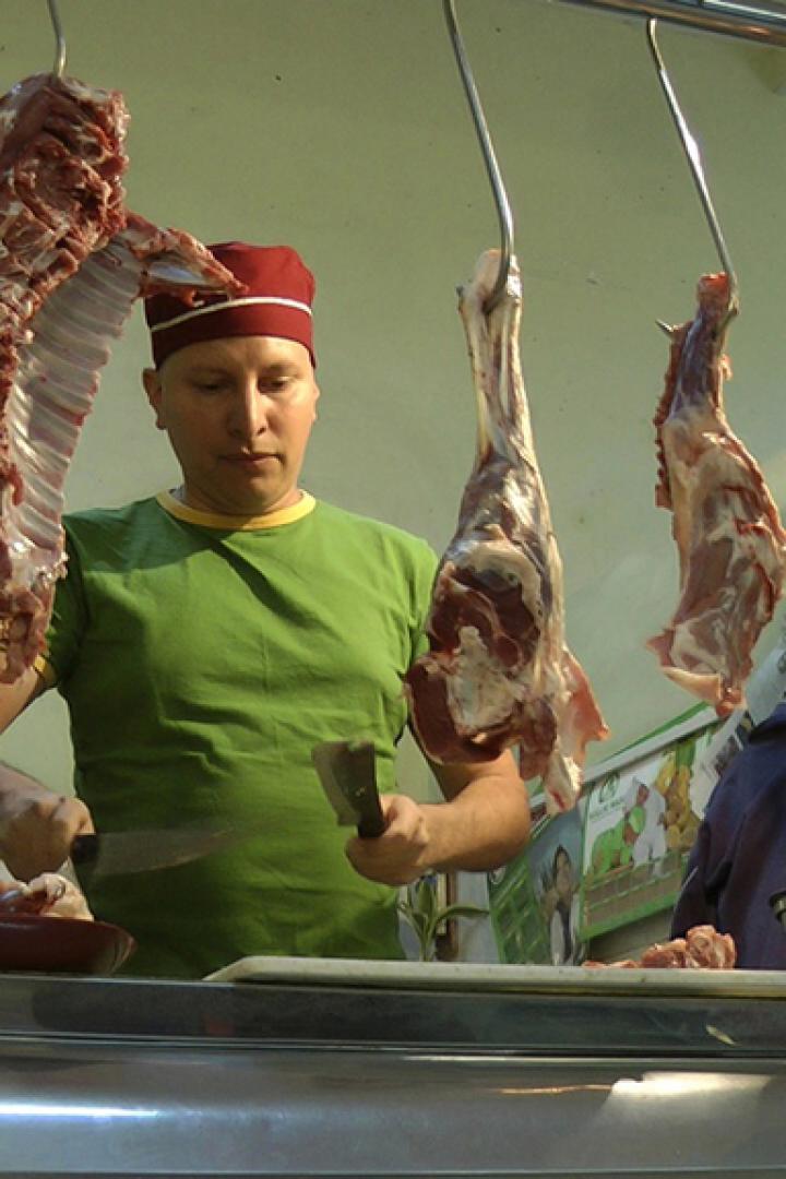 Ein Metzger mit roter Mütze zerteilt Fleisch in einem Schlachtbetrieb.