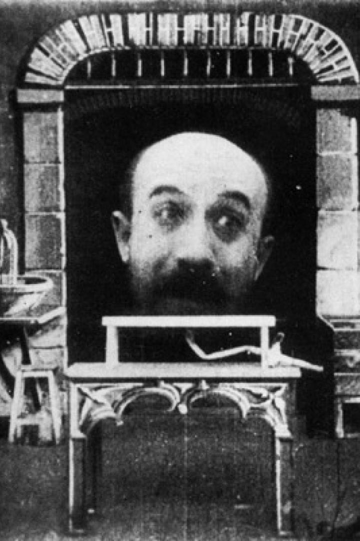 Ein Mann sitzt vor einer riesigen schwebenden Kopfattrappe in einem Filmstudio.