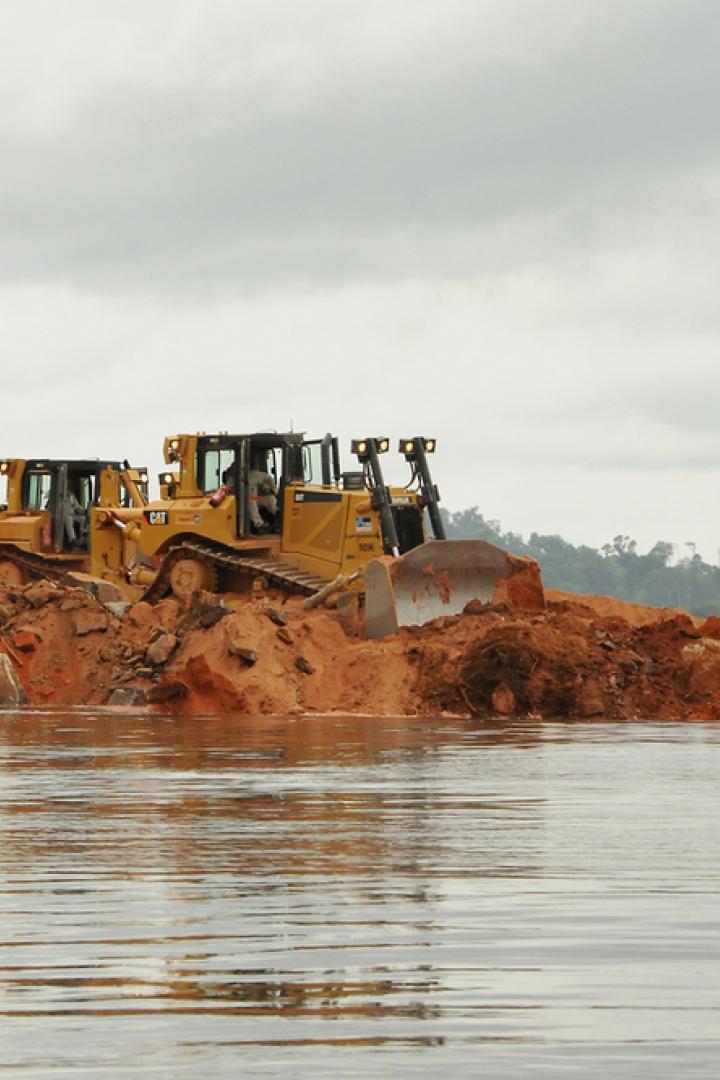 Zwei gelbe Bulldozer schieben Erde in einem Gewässer zusammen.