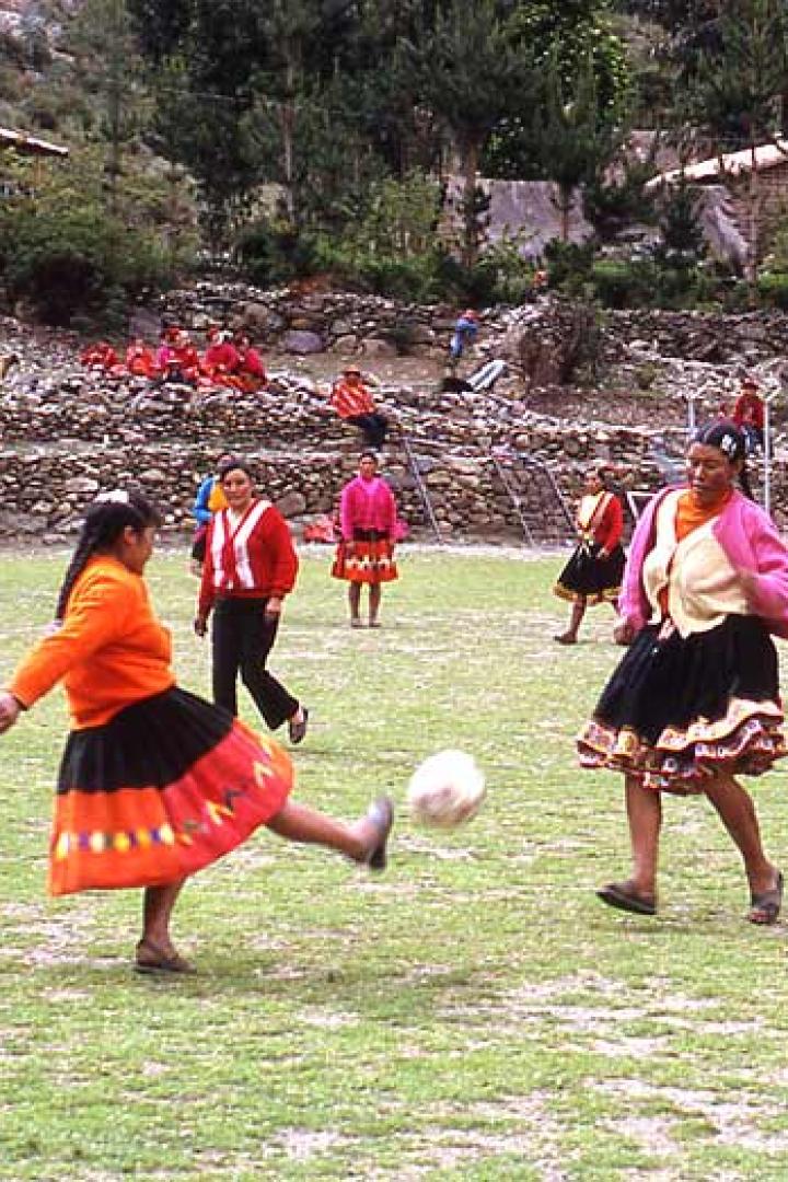 Frauen in traditioneller Kleidung spielen Fußball auf einem grünen Feld.
