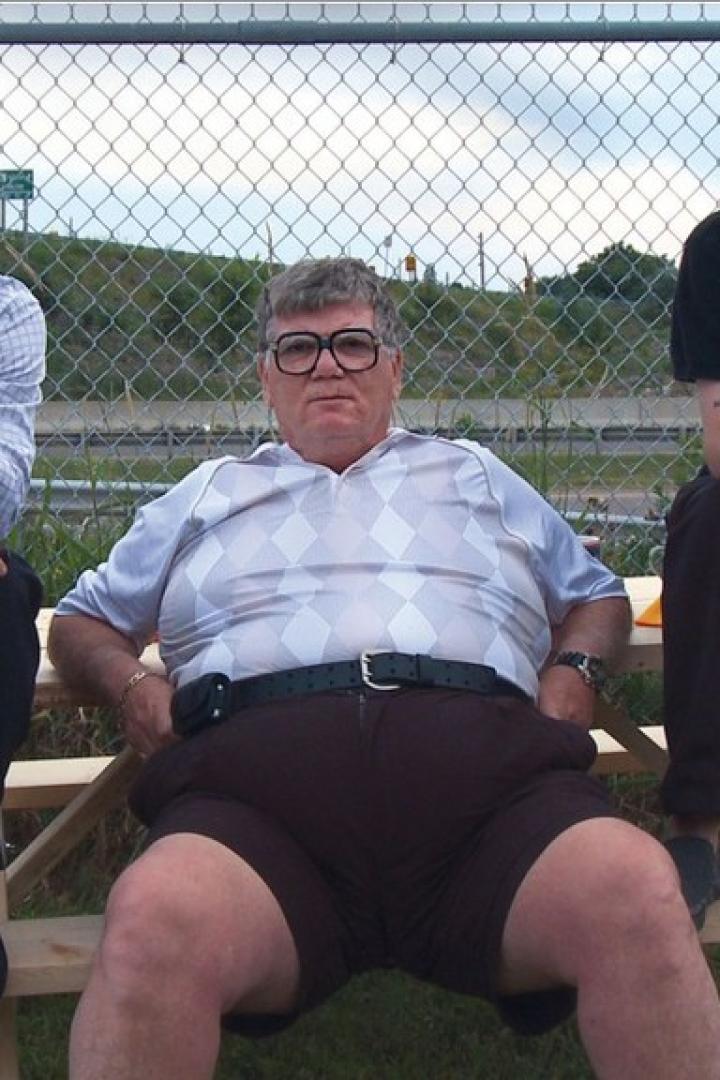 Drei Männer sitzen auf einer Picknickbank vor einem Zaun.