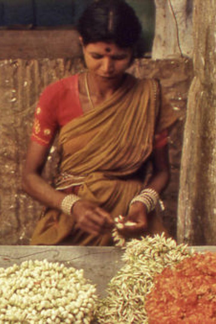 Eine Frau in einem Sari fertigt Blumengirlanden an einem Stand.