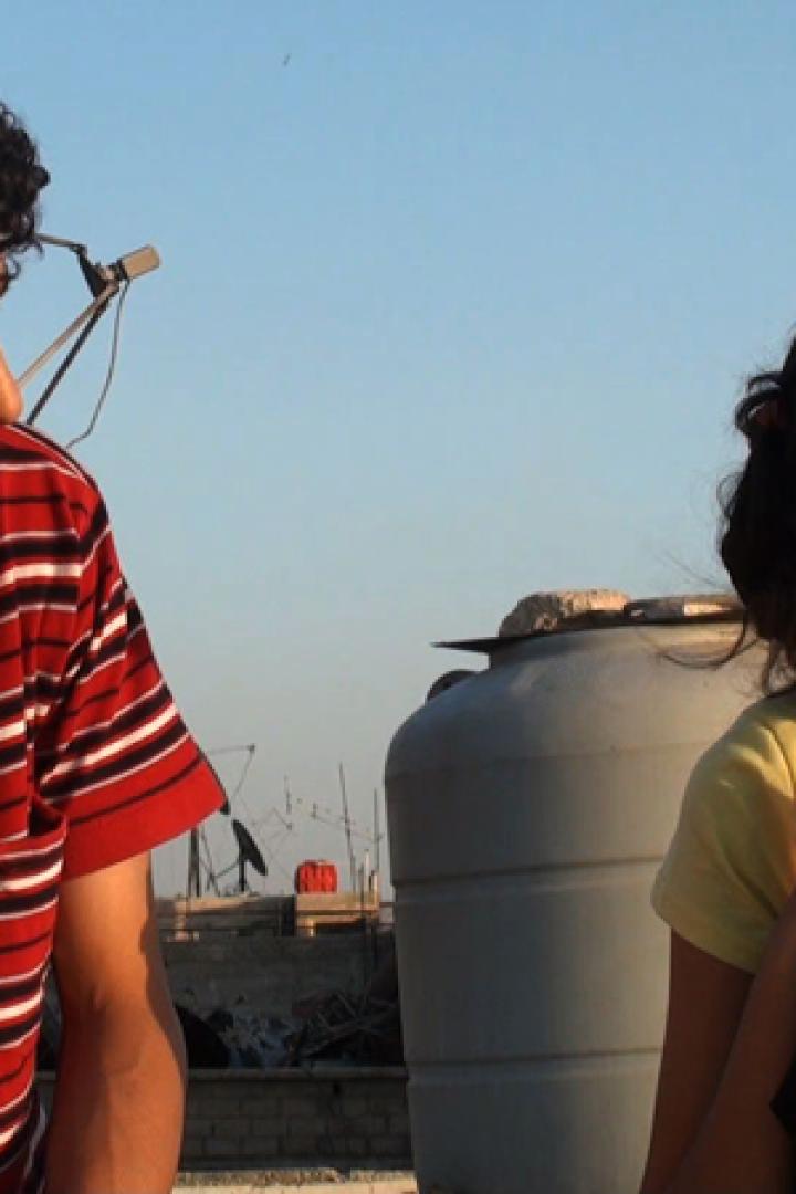 Ein junger Mann und eine junge Frau sitzen auf einem Dach und schauen in die Ferne.