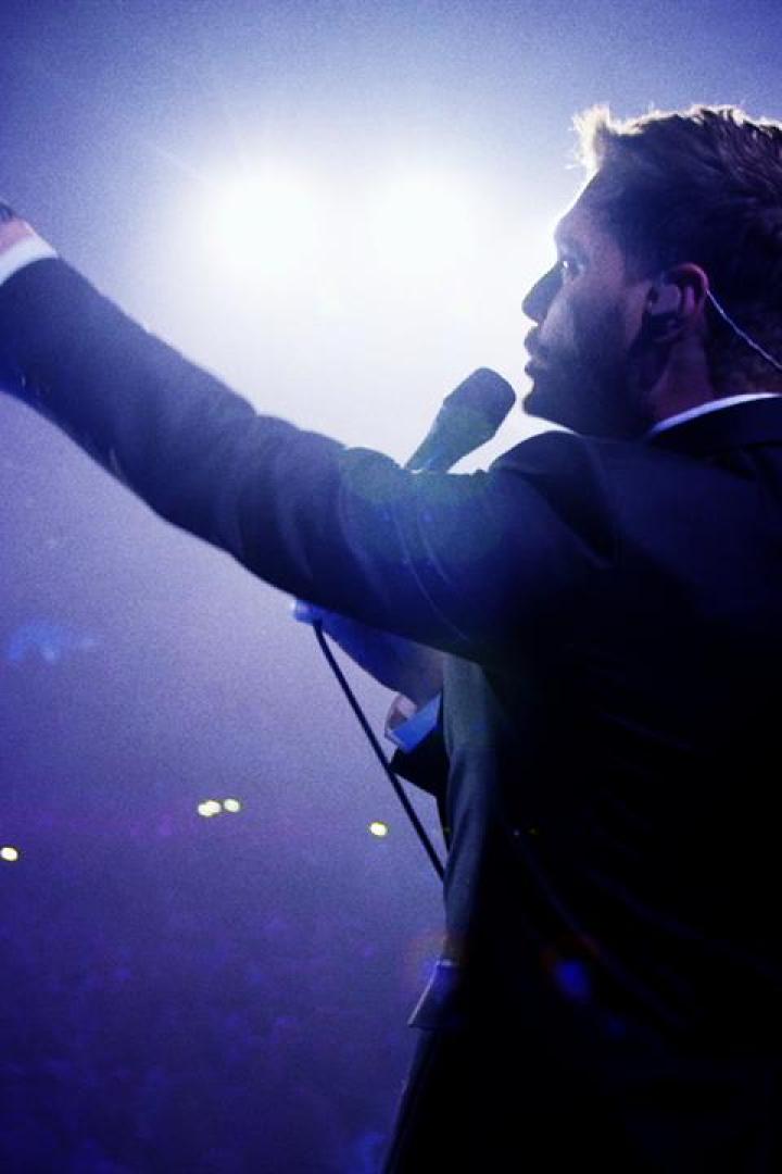 Ein Mann in einem Anzug steht auf einer Bühne und zeigt mit dem Finger nach oben.