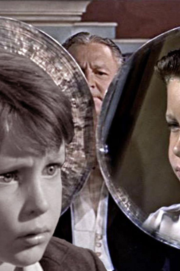 Zwei Jungen sind durch kreisförmige Spiegel zu sehen, im Hintergrund ein Mann.