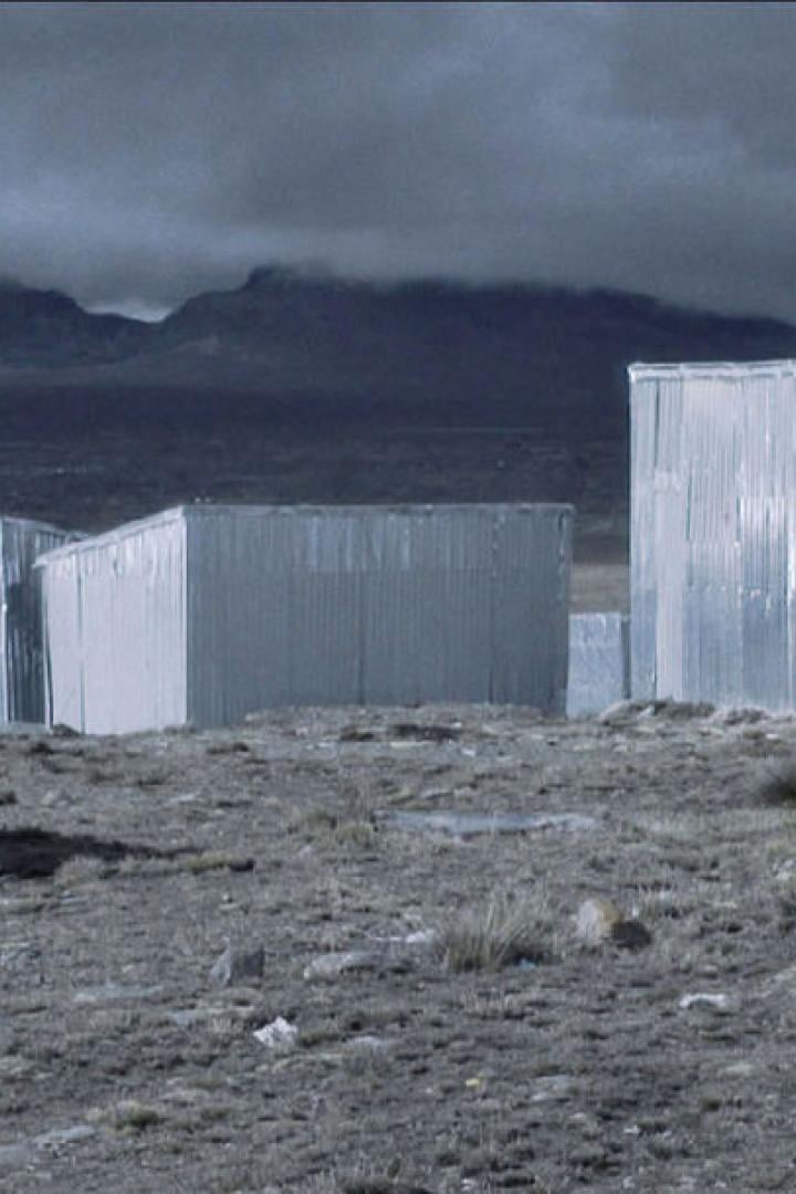Mehrere kleine Gebäude aus Wellblech in einer kargen Landschaft unter einem dunklen Himmel.