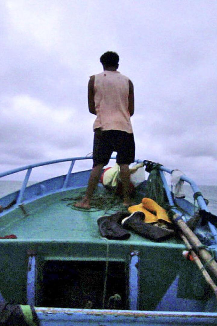 Ein Mann steht auf einem kleinen, blauen Boot auf dem offenen Meer.
