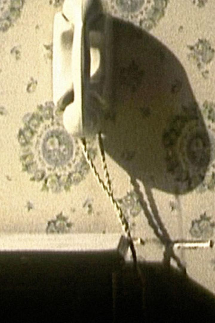 Ein altmodisches Telefon hängt an einer Wand mit Blumenmuster neben einem Nachttisch.