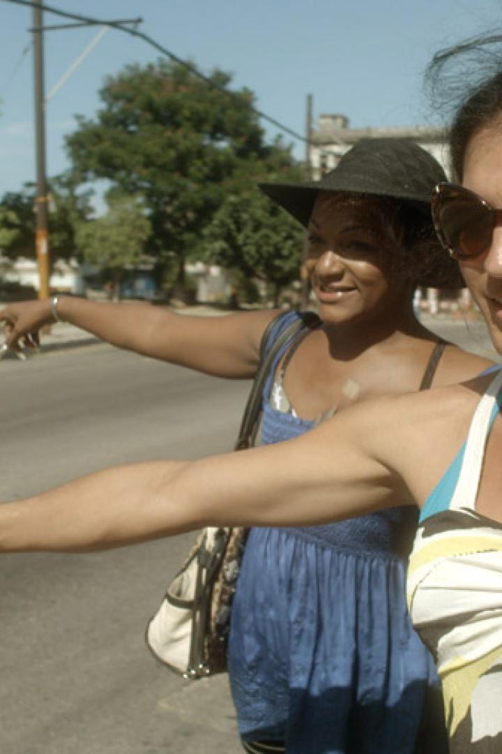 Zwei Frauen stehen an einer Straße und zeigen in die Ferne.