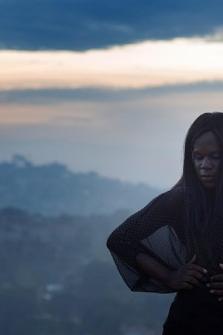 Eine Frau steht vor einer verschwommenen Landschaft im Abendlicht.
