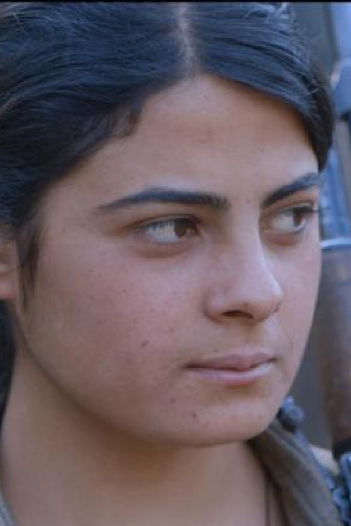 Eine junge Frau mit einem Gewehr über der Schulter blickt entschlossen zur Seite.