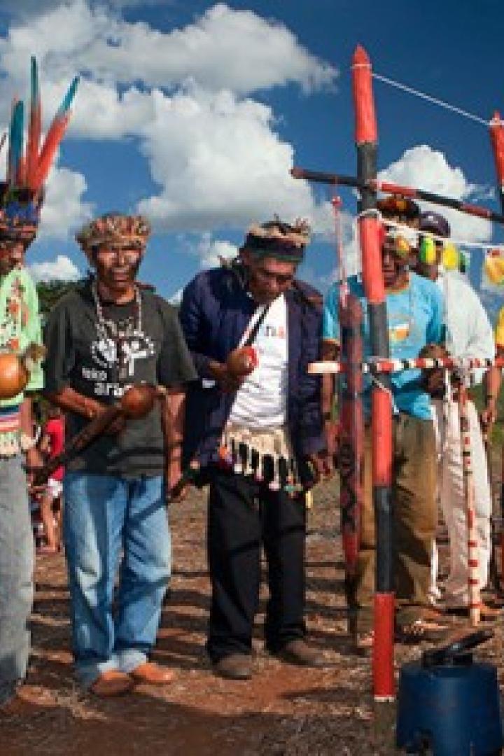 Eine Gruppe indigener Männer hält Kürbisse und trägt traditionelle Kopfbedeckungen.